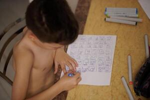 Top view of boy at table drawing comics and cartoons on white sheet of paper photo