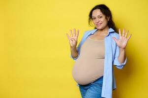 Cheerful pregnant woman expecting a baby, showing number nine with her fingers, 9 month of happy carefree pregnancy photo