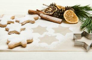 Baked star-shaped gingerbread cookies powdered with sugar for Christmas on baking parchment paper near pine cones and twigs, dried orange slices and cinnamon sticks photo