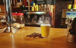 Yellow takeaway cup with hot coffee and scattered roasted beans on a wooden table on the background of coffee machine photo