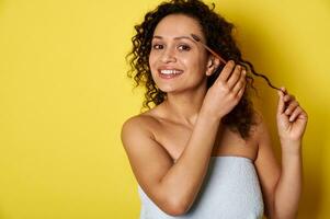 sonriente mezclado carrera joven mujer con Perfecto piel y maquillaje posando con maquillaje cepillo terminado amarillo antecedentes foto