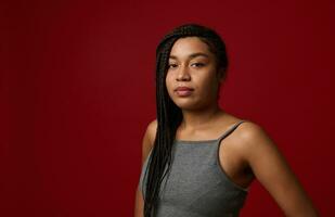 Portrait of a charming young African American beautiful woman with stylish traditional dreadlocks, confidently looking at camera, isolated over red background with copy space photo
