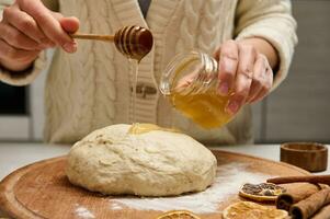 Close-up woman preparing gingerbread dough, holding a wooden dipper and pouring some honey on pastry photo