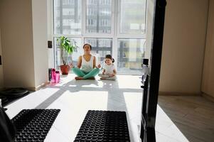 relajado mujer medita con su hija mientras practicando yoga en el Mañana a hogar. foto