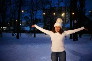 Young happy woman enjoying winter evening in the park on the background of lights and snow covered nature photo