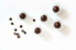 Flat lay with chocolate truffles sprinkled with freeze-dried strawberries in paper wrappers and scattered chocolate pills on white background with copy space. Concept of chocolate day photo