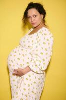 Confident serious pregnant woman in summer sundress, expecting a baby, holding belly and looking at camera photo