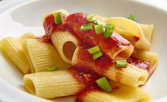 Close-up food photography of a cooked traditional Italian dish on a plate - whole wheat pasta - tortiglioni with tomato sauce and green onion garnish photo