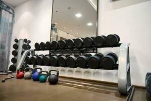 Close-up many metal dumbbells and kettlebells on rack in sport fitness center on the background of large mirrr in fitness club photo