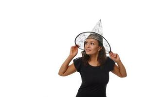 Isolated portrait on white background of an attractive young woman smiling with beautiful toothy smile, wearing a witch wizard hat and looking at the side on a copy space for Halloween advertisement photo