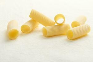 Studio shot with soft shadow of raw Italian pasta- whole wheat tortiglioni on white background with scattered flour. Copy space for ad. Food photo