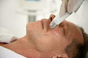 Close-up of a handsome mature European man receiving professional skin care treatment in wellness spa center. Modern medical equipment for anti-aging, revitalizing and rejuvenating treatment photo