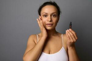 Beautiful middle aged woman holds a jar with beauty product, applies it on her face and performs anti-aging lymphatic drainage massage for rejuvenation and skin smoothing. SPA, cosmetology concept photo