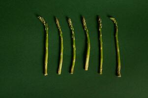 Monochrome flat lay food composition of green organic asparagus on dark green background with copy space. Healthy raw vegan food photo