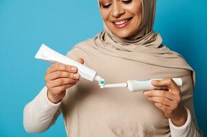 Close-up woman with a beautiful smile squeezes toothpaste from a tube into a toothbrush photo