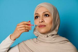 de cerca de hermosa musulmán mujer en hijab participación un jeringuilla con belleza inyección cerca su labios. labios aumento concepto en inyección cosmetología foto