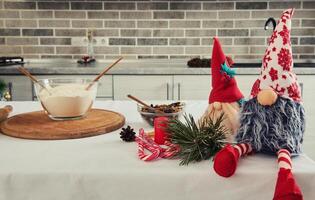 Close-up of handmade Scandinavian gnomes, candy canes and red candles on a table next to a bowl with flour and dried fruits for preparing Christmas cake - shtoelen photo