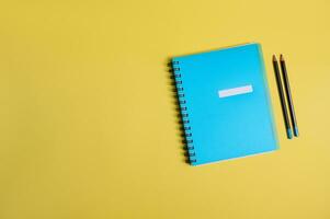 Flat lay of a blue colorful notepad, organizer and two pencils, on yellow background with space for text. Back to School and Teachers' Day, office and business, time management, planning concepts photo