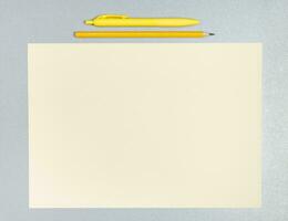 plano laico composición de amarillo bolígrafo, lápiz y sábana de papel en un gris superficie foto