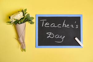 Flat lay composition of a beautiful bouquet of autumn asters flowers in craft wrapping paper tied with a rope and blackboard with inscription Teachers Day on a yellow background with space for text photo