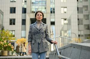 Confident brunette woman walking along the street on the background of modern corporate buildings photo