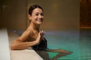 Portrait of a beautiful middle aged Caucasian woman relaxing in swimming thermal pool in luxury wellness spa resort. Purity, hydrotherapy, recreation, healthy and active lifestyle concept. Copy space photo