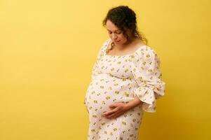 grávido mujer suavemente acariciando su grande barriga terminado amarillo fondo, Copiar espacio. el embarazo 40 semana. parto concepto foto