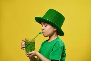 pequeño chico bebidas desde un Paja con trébol hoja ornamento un verde bebida celebrando un Santo patrick's día. Copiar espacio foto