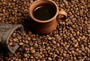 High angle view of a clay coffee cup with freshly brewed coffee drink with steam on the background of a bag with grains and freshly roasted coffee beans . Copy space for advertising. Still life photo