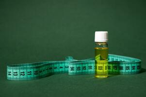 Still life with a glass vial of massage anti cellulite oil and measure tape, isolated on green background photo