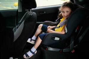 bebé niña ceñido en un la seguridad niño coche asiento, sonrisas mientras mirando a el cámara. utilizando un niño coche asiento a viaje sin peligro con niños en un coche foto