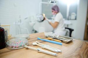 Dentistry. Dental practice. Modern dental tools, sterile stainless steel instruments on a wooden surface against a blurred background of a dentist treating caries to a patient in a dental office photo