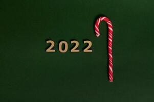 Conceptual tudio shot of wooden numerals 2022 and sugary striped white and red Christmas lollipop, sweet candy cane, symbolizing New year and Christmas traditional event with space for advertisement photo