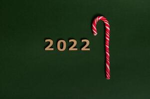 Conceptual tudio shot of wooden numerals 2022 and sugary striped white and red Christmas lollipop, sweet candy cane, symbolizing New year and Christmas traditional event with space for advertisement photo