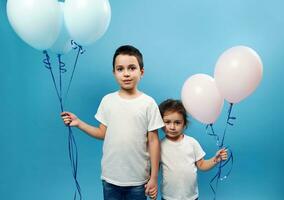 Boy and girl stand side by side holding each other's hands and colored pink and blue balloons in the other hand. Child protection concept. Happy childhood photo