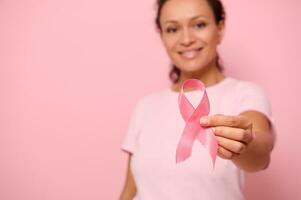 Blurred smiling African woman in pink t-shirt holding satin ribbon in her hand. Breast and abdominal cancer awareness, October Pink day on colored background, copy space. Breast cancer support concept photo