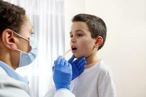 joven pediatra examinando pequeño Niños garganta a diagnosticar su enfermedad. foto