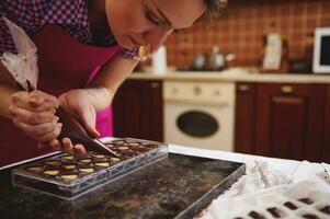 Chef chocolatier squeezing filling of creamy liquid preparing luxury handmade chocolate pralines at home kitchen photo