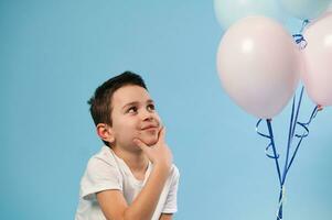 un linda chico astutamente y pensativamente mira a un globo en un azul antecedentes foto