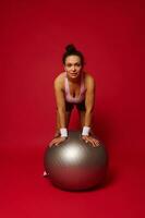 Portrait of a beautiful athlete woman with a fit ball isolated over red background with copy ad space photo