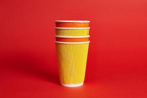 Stack of multicolored paper disposable cups for hot drinks on a red background with copy space. photo