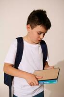 Serious teenage schoolboy in white mockup t-shirt and blue jeans, holding copybooks, isolated on white studio background photo