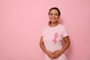 Smiling mixed race woman in pink T-shirt with pink satin ribbon symbolizing International Breast Cancer Day, expressing solidarity and support for breast cancer patients and survivors. 1 st october photo