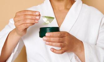 Cropped image of female hands holding jar and taking collagen under eyes patches out of it, isolated on beige background with copy space photo