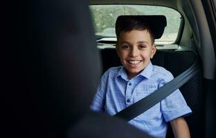 Shot through the driver seat of a smiling boy fastened with seatbelt while travelling by car in safety child car seat photo