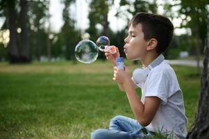 adorable hermoso preadolescente niño chico soplo comenzando jabón burbujas en el parque, descansando durante su colegio recreación foto