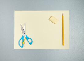 Eraser, pencil and scissors on a yellow sheet of paper. Top view, flat lay photo