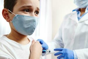 Terrified boy vaccinated on background of blurred doctor in gloves and white medical gown photo