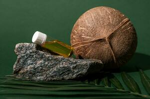 Still life with coconut and glass vial with cosmetic oil displayed on stone and palm leaf, isolated on green background photo