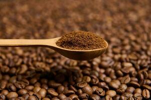 Close-up of a wooden spoon with ground coffee the background of scattered fresh roasted coffee beans with copy space for advertisement. Still life photo